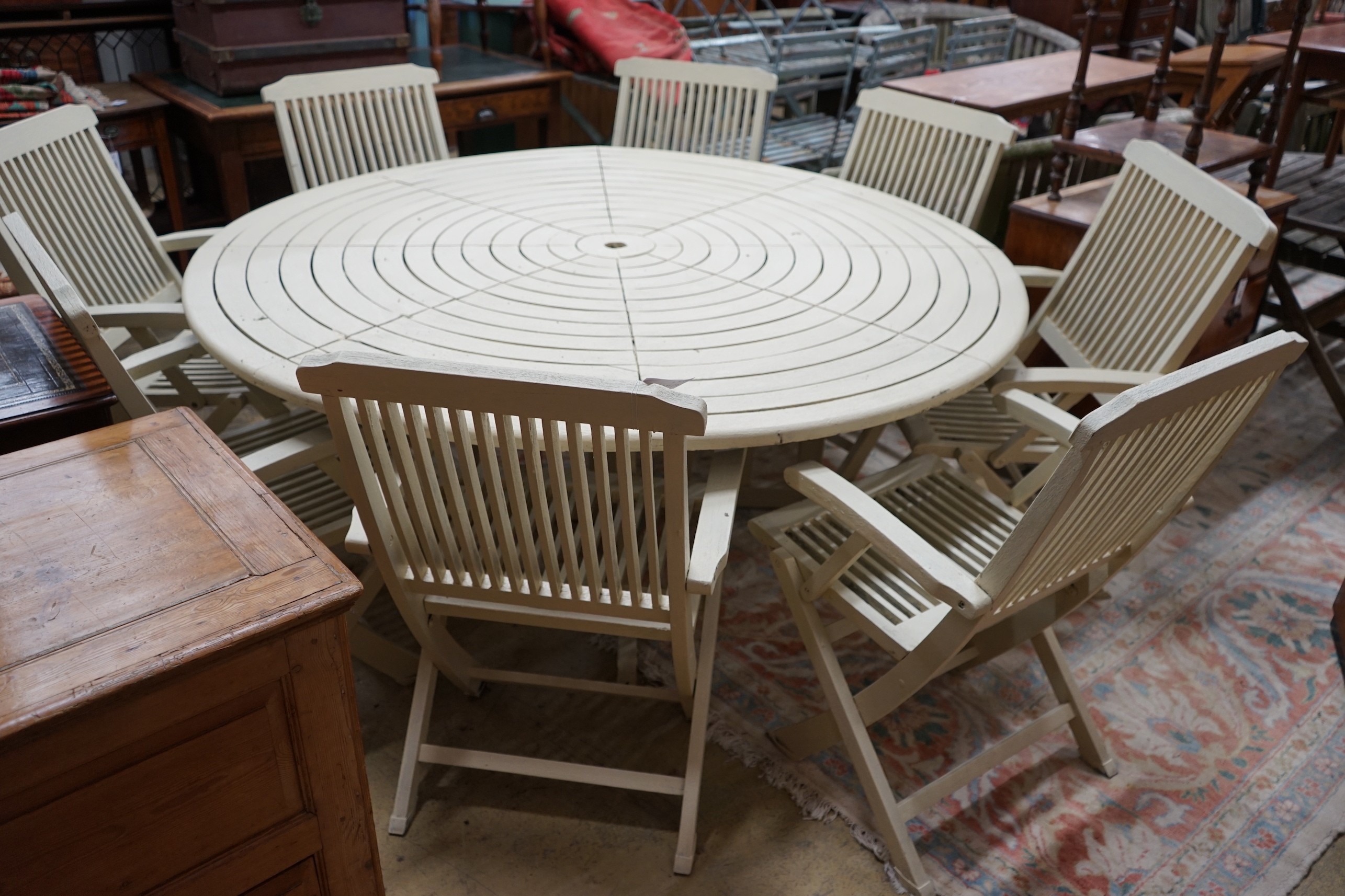 A circular painted teak garden table, diameter 180cm, height 72cm and eight matching folding garden elbow chairs